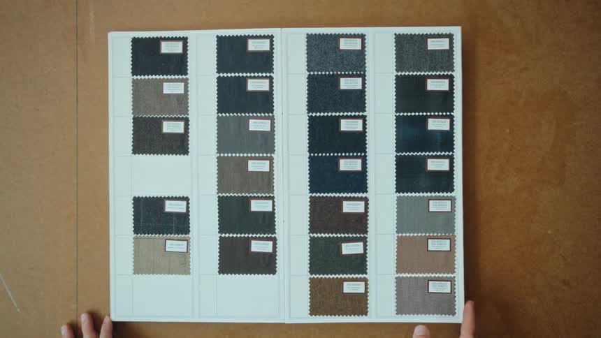 Top-down view of hands flipping through a book of suiting fabric swatches in a tailor's workshop