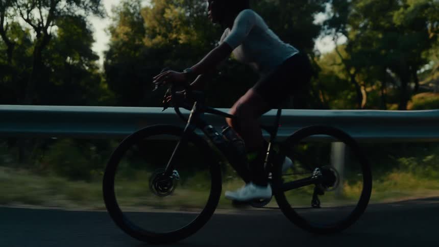 Slow motion tracking shot of a female cyclist riding her bike on a scenic road at sunset