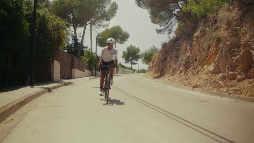 Low-angle view of a cyclist in full gear speeding down a sunny, tree-lined suburban road
