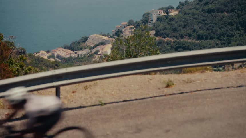 A motion-blurred cyclist speeds down a winding coastal road on a sunny day with the ocean in the background
