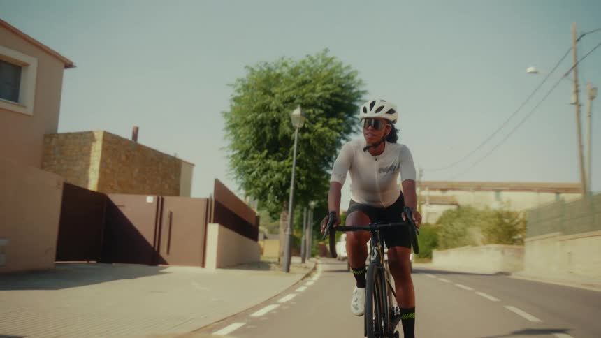 A determined woman in professional gear cycles down a quiet residential street on a sunny day
