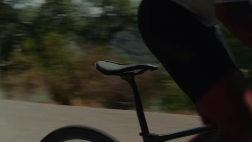 A close-up slow-motion tracking shot follows a cyclist riding a road bike along a scenic country road