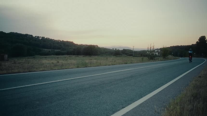Motion blur of a professional cyclist riding a road bike down a country highway at dusk