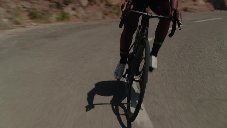 Slow motion, front-facing view captures an athletic man cycling along a winding paved road on a sunny day