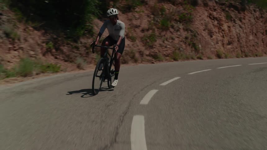 A determined female cyclist in full gear rides her road bike up a winding mountain road on a sunny day