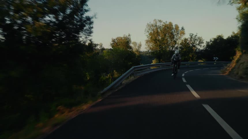 A professional road cyclist rides up a challenging winding mountain road during golden hour