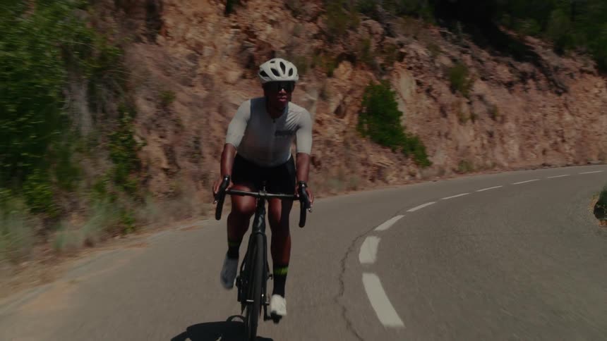 An athletic woman cycles up a winding mountain road during a sunny day training session