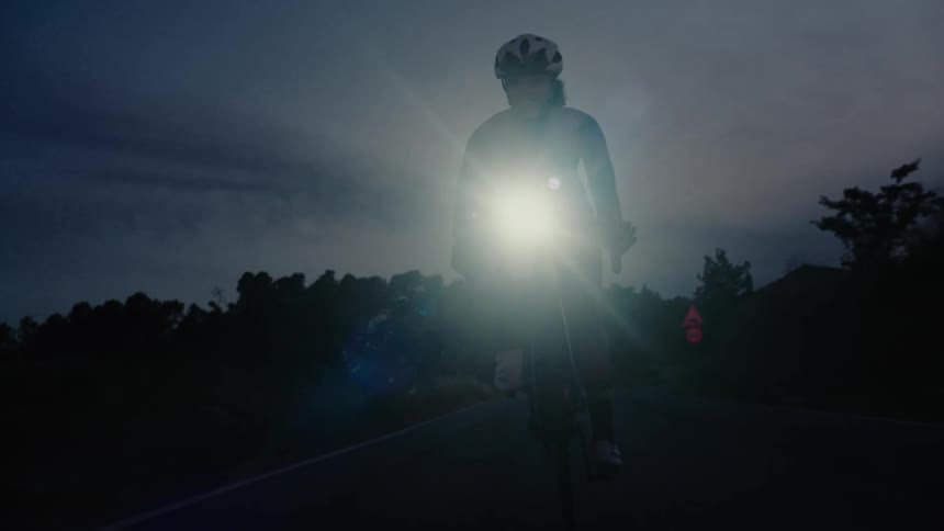 Silhouette of a cyclist riding on a dark road at dusk with a bright flashing headlight and tail light for safety