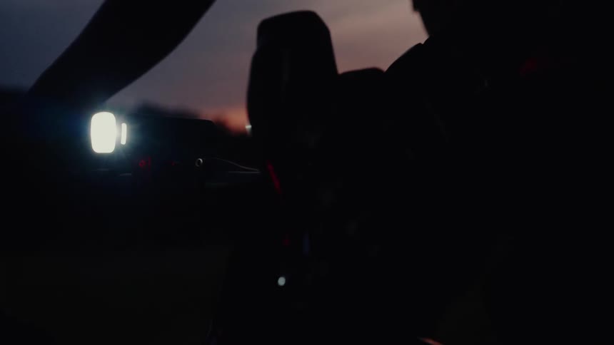 Close-up of a cyclist's hands on the handlebars with a bright headlight on while riding at dusk