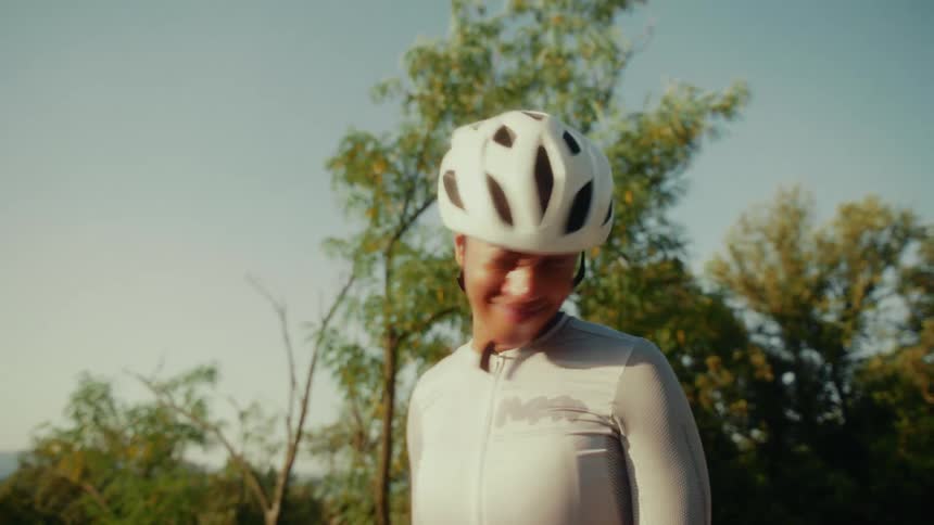 A smiling female cyclist in a helmet takes a moment to rest and enjoy the sunny day outdoors