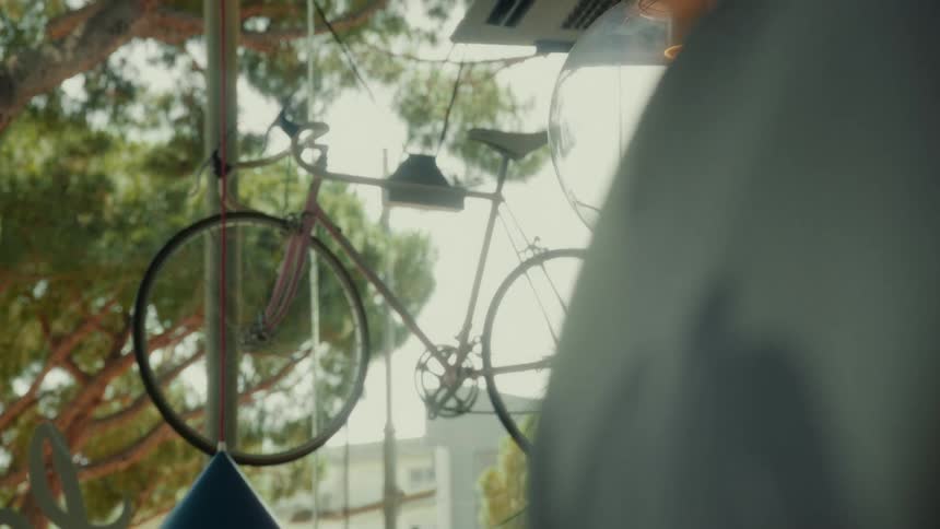 A vintage pink bicycle hangs as a decoration in a sunny shop window next to a glowing light fixture