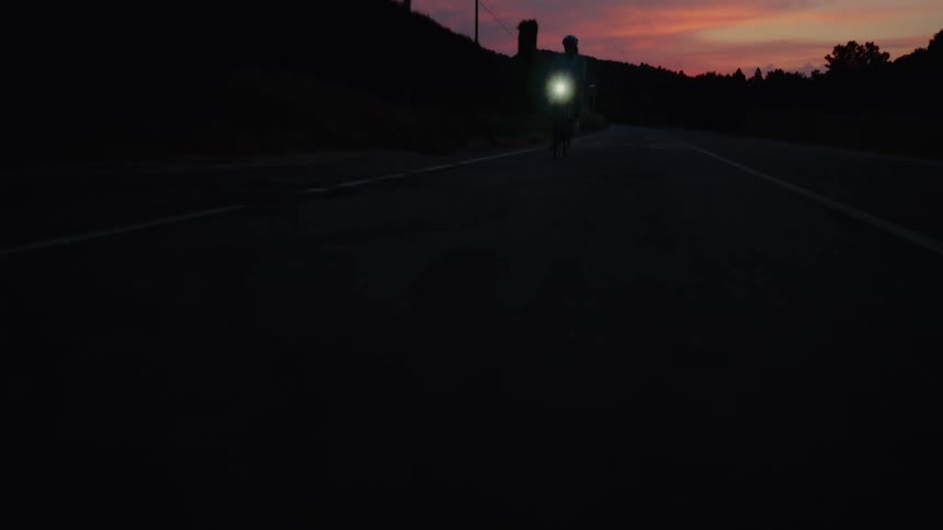 Dramatic low-angle pull-back shot reveals a cyclist riding on an empty road during a colorful sunset