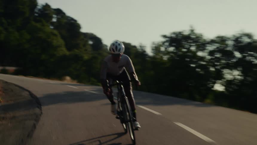 An athletic man in slow motion cycles with determination up a winding mountain road on a sunny day