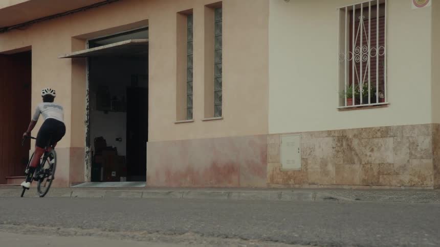 Slow motion shot of a cyclist in full gear riding her road bike down a town street and into an open garage