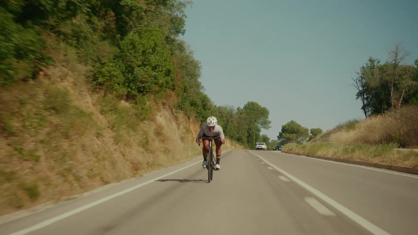 Front view of a professional cyclist riding fast down an empty country road on a sunny day