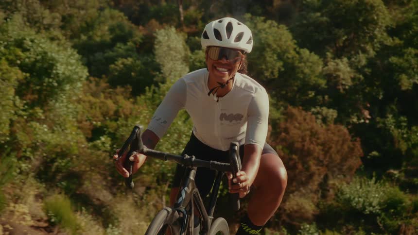 Portrait of a smiling professional female cyclist riding her road bike up a sun-drenched hill