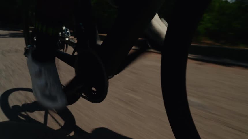 Close-up shot of a cyclist's feet pedaling a road bike on a paved road during a sunny day