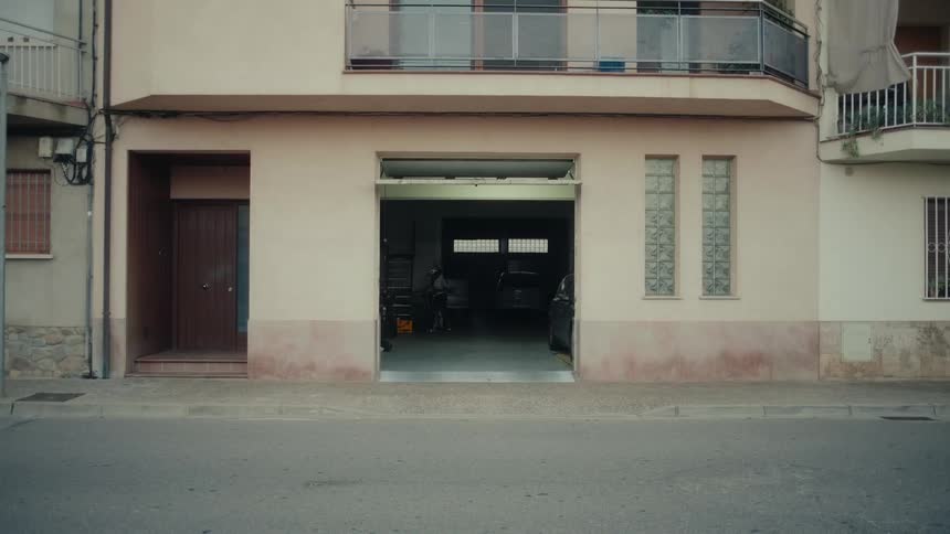 A wide, static shot of a quiet street with an open garage on the ground floor of a residential building