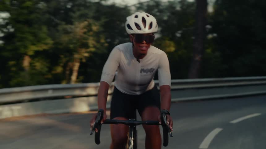 A determined female cyclist rides up a winding forest road as the sun sets