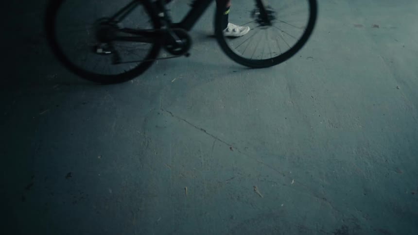A close-up of a bicycle's wheels as they roll across a dusty, teal-colored concrete floor
