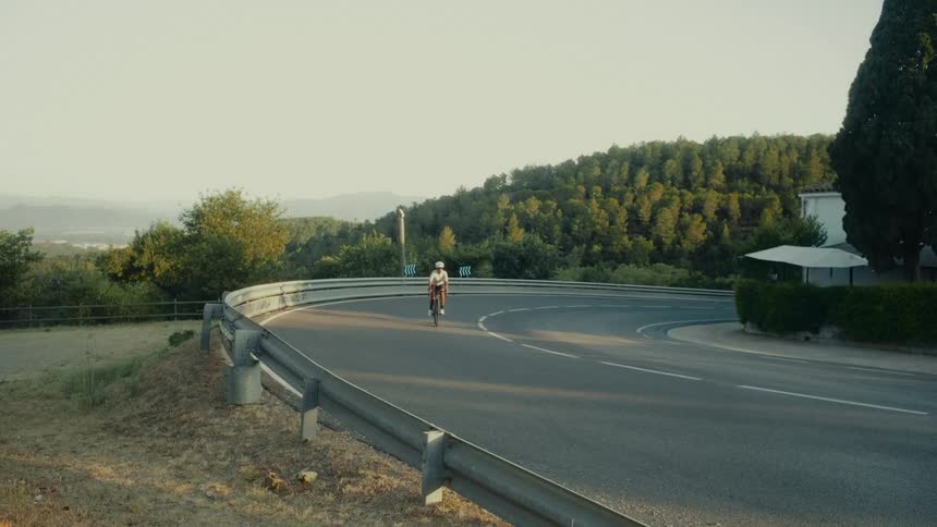 A lone cyclist navigates a sharp curve on a scenic mountain road during golden hour