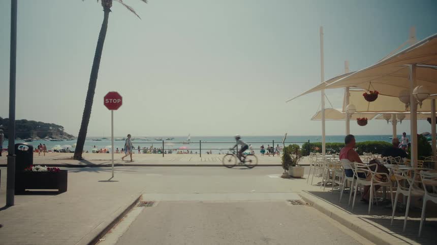 A sunny day at a beachside resort with people relaxing at a cafe, walking, and cycling along the promenade