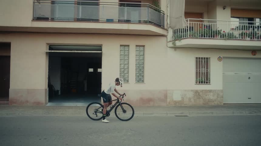 Slow motion shot of a professional cyclist getting on a bike and riding away from their home for a training session