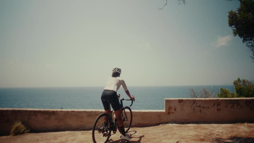 A female cyclist rides her bike to a scenic coastal overlook and stops to admire the beautiful ocean view on a sunny day