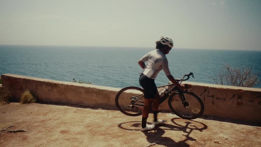 A cyclist takes a break from her ride to stretch and admire the beautiful ocean view from a sunny cliffside viewpoint in slow motion