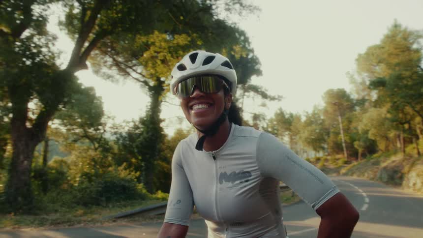 Close-up portrait of a happy female cyclist in a helmet and sunglasses smiling while riding on a scenic road at sunset