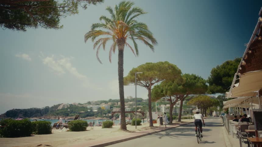 A female cyclist rides her bicycle down a beautiful coastal promenade next to a sandy beach on a sunny day