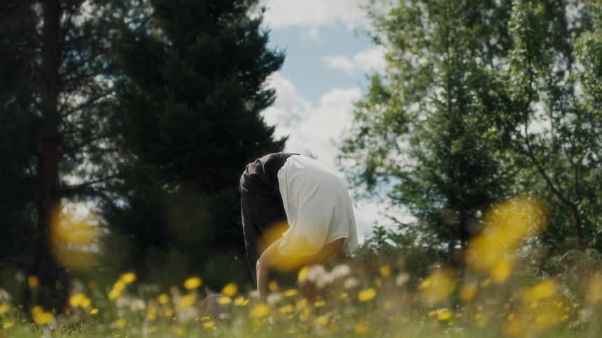 A woman with red hair slowly unrolls her spine while stretching in a beautiful field of wildflowers on a sunny day