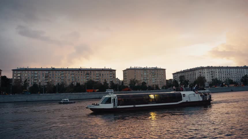 A passenger boat travels along a river in a European city during a beautiful, calm sunset