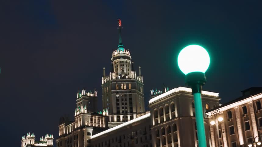 The majestic Kudrinskaya Square Building in Moscow stands illuminated against the dark night sky, framed by a glowing green street lamp