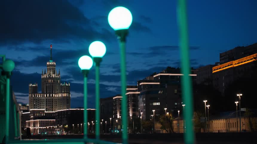 An illuminated Stalinist skyscraper on the Moscow River embankment is seen through glowing green lights at twilight