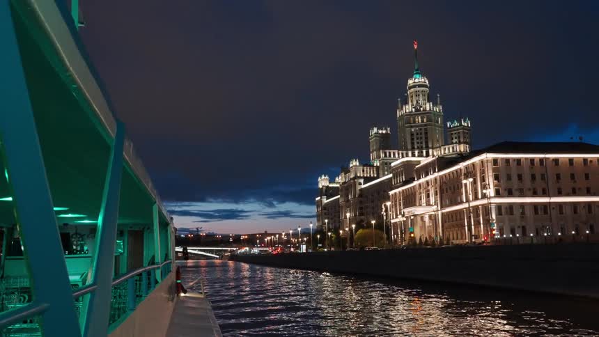 A boat floats along the Moskva River at night, offering a picturesque view of the illuminated Kotelnicheskaya Embankment Building