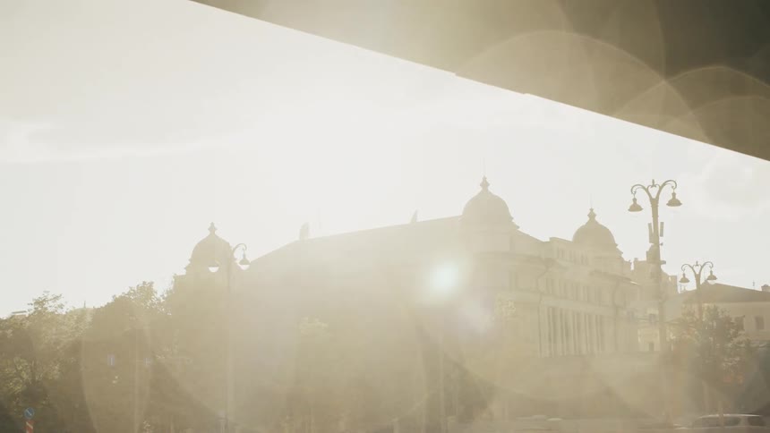 Sunlight flares over a historic city building as seen from beneath a bridge