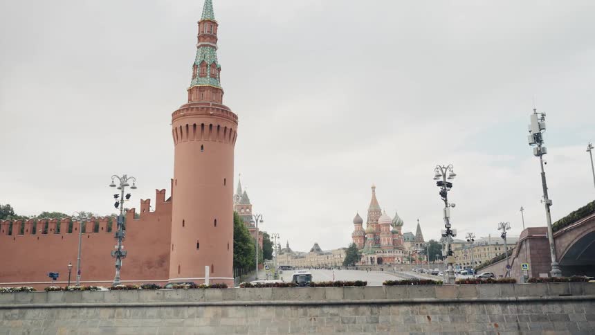 A slow reveal of the Moscow Kremlin's Beklemishevskaya Tower and St. Basil's Cathedral from the Moskva River on a cloudy day