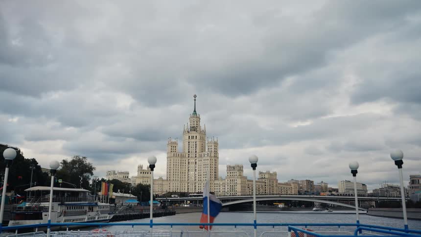 A Russian flag waves on a boat sailing on the Moskva river with a view of the grand Kotelnicheskaya Embankment Building on a cloudy day