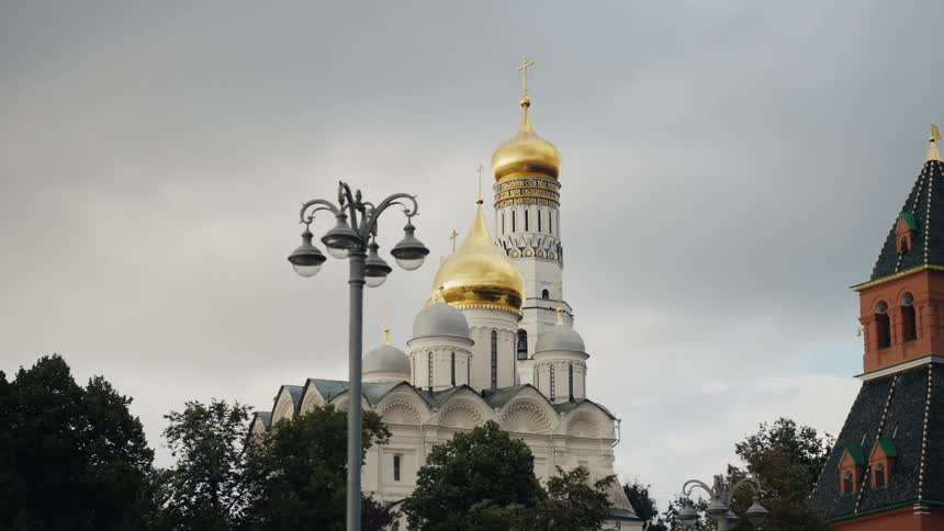 A slow pan reveals the majestic Ivan the Great Bell Tower and its golden domes within the Moscow Kremlin on a cloudy day