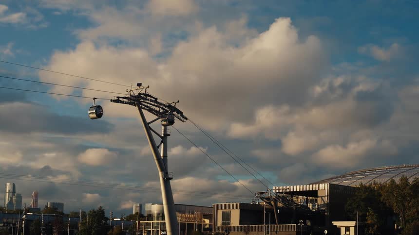 Modern gondola cars glide over the city against a backdrop of skyscrapers and a dramatic cloudy sky at sunset