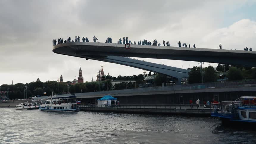 Tourists enjoy panoramic city views from the modern floating bridge in Moscow's Zaryadye Park on a cloudy day