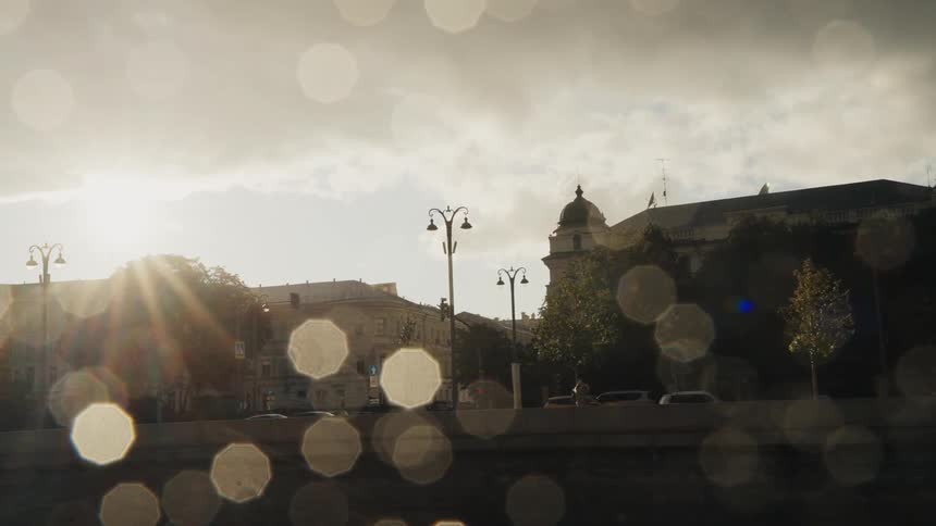 Passing by a sunlit European city waterfront on a river with a dreamy bokeh effect from raindrops