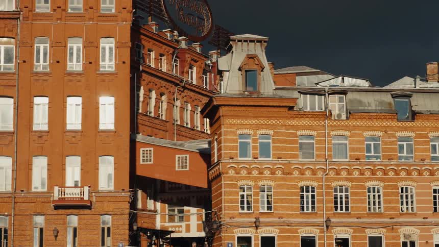 A slow pan reveals the ornate red brick facade of historic industrial buildings, illuminated by the sun against a dark, stormy sky