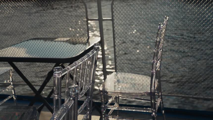 Close up of empty acrylic chairs on a boat deck as the sun sparkles on the passing water