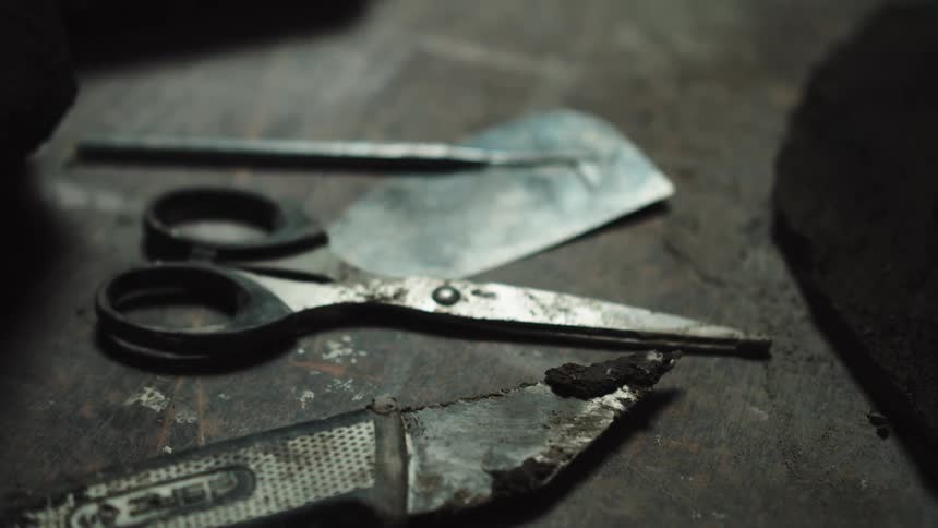 A gritty close-up shot of various old and dirty hand tools resting on a dusty workbench in a workshop