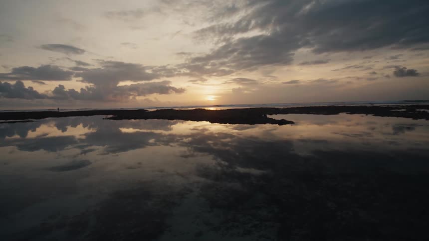 A serene sunset over the ocean is perfectly reflected in the calm, still waters of the tide pools