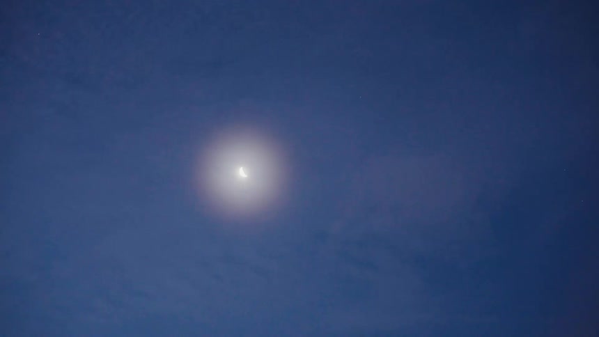 A beautiful crescent moon glows with a soft halo against the deep blue night sky