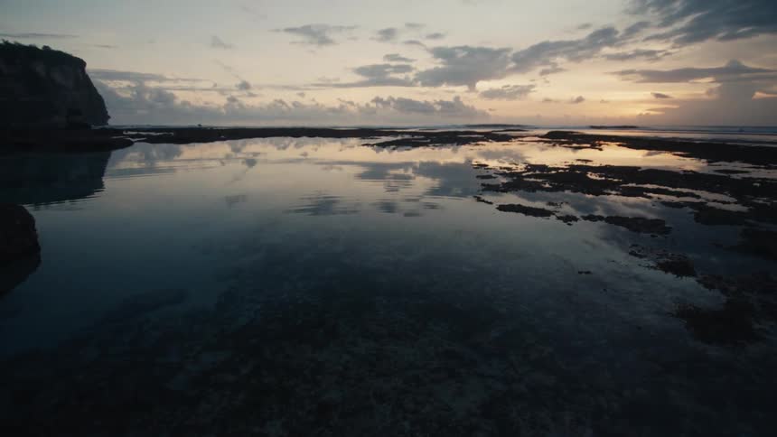 A tranquil tide pool reflects the dramatic sunrise sky along a rocky coastline