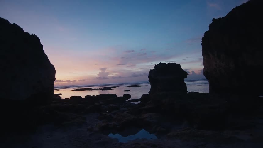 Silhouetted rock formations frame a tranquil ocean view under a colorful twilight sky